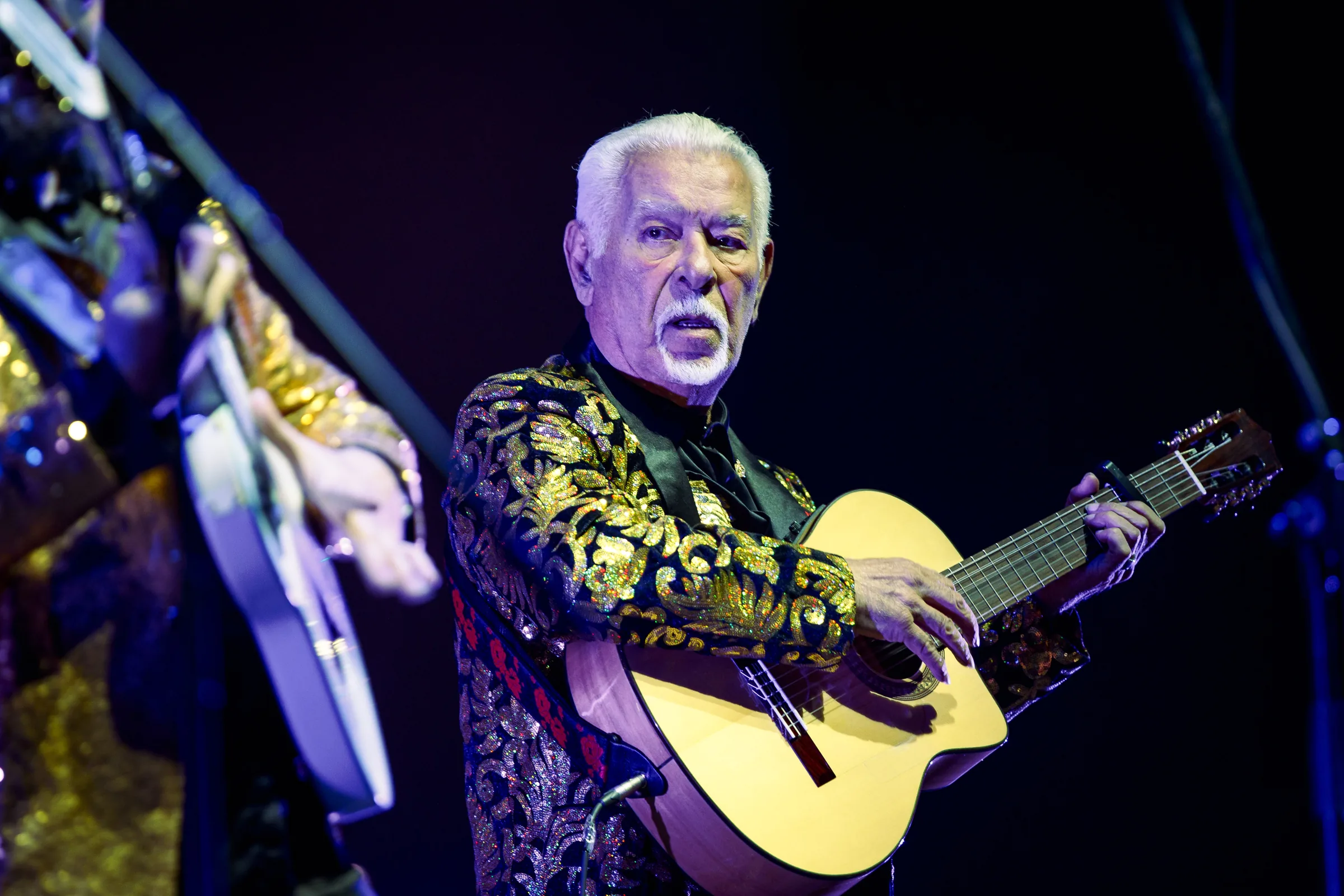 Paul Reyes in concerto con chitarra e giacca dorata